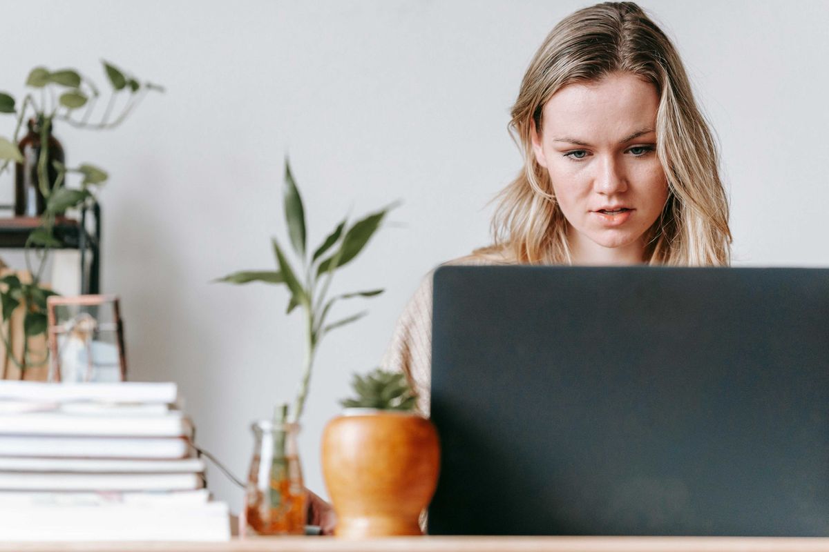 Woman focused on laptop at desk with plants and books.