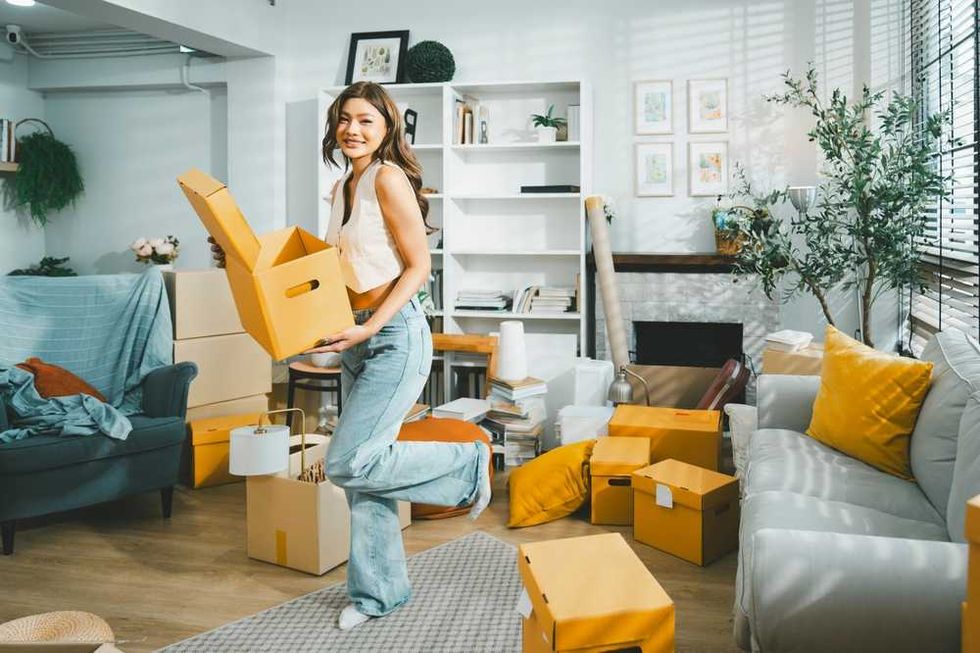 Woman happily unpacking boxes in a sunlit, cozy living room.