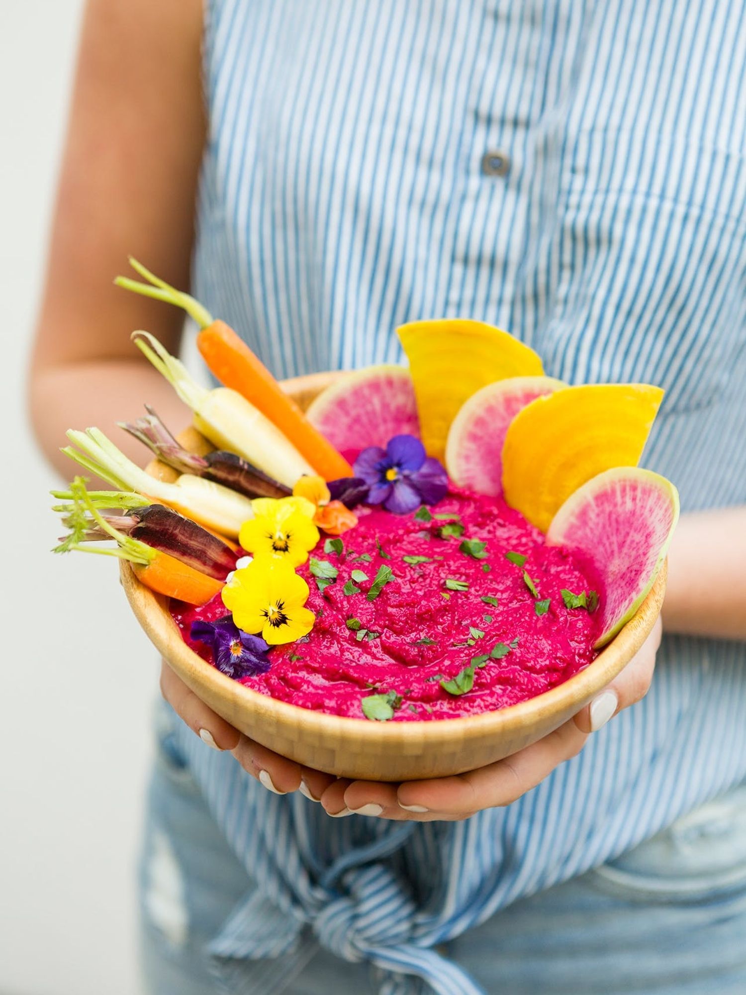 Woman holding a bowl of Beet Hummus decorated with flowers and carrots