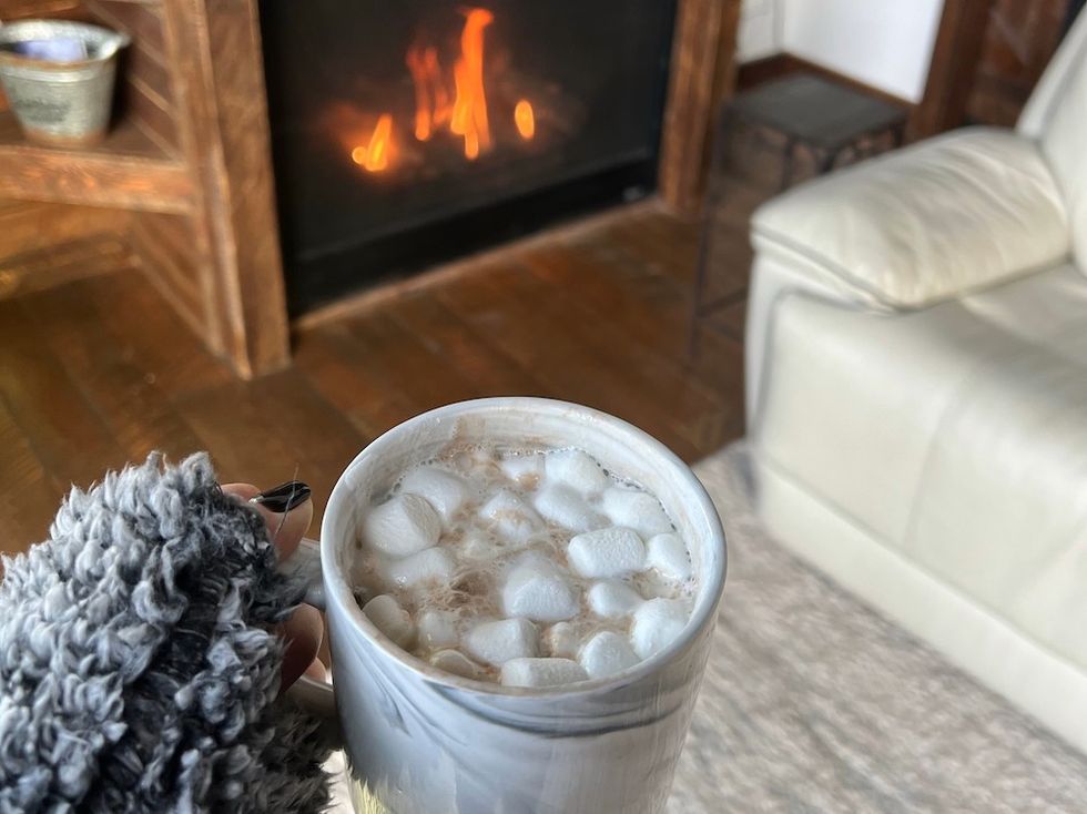 woman holding a cup of hot chocolate with marshmallows by a fire