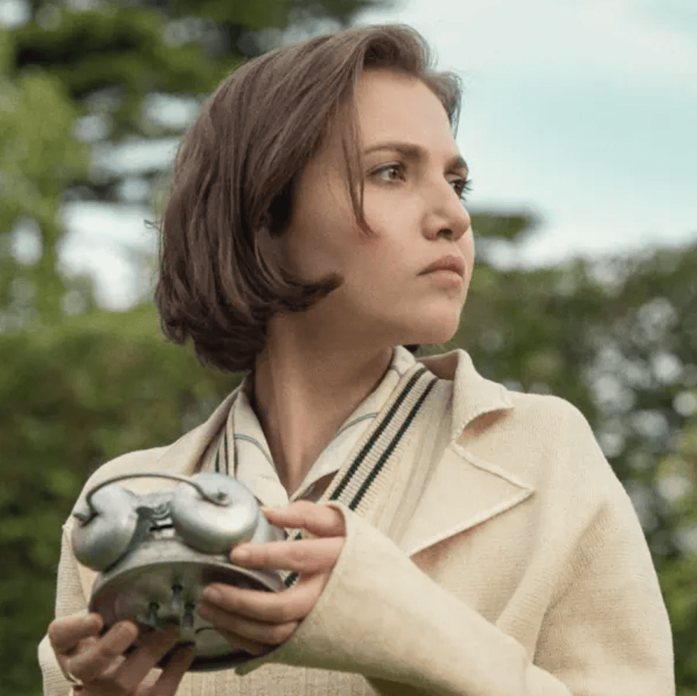 Woman holding a metal device, looking to the side, with greenery in the background.