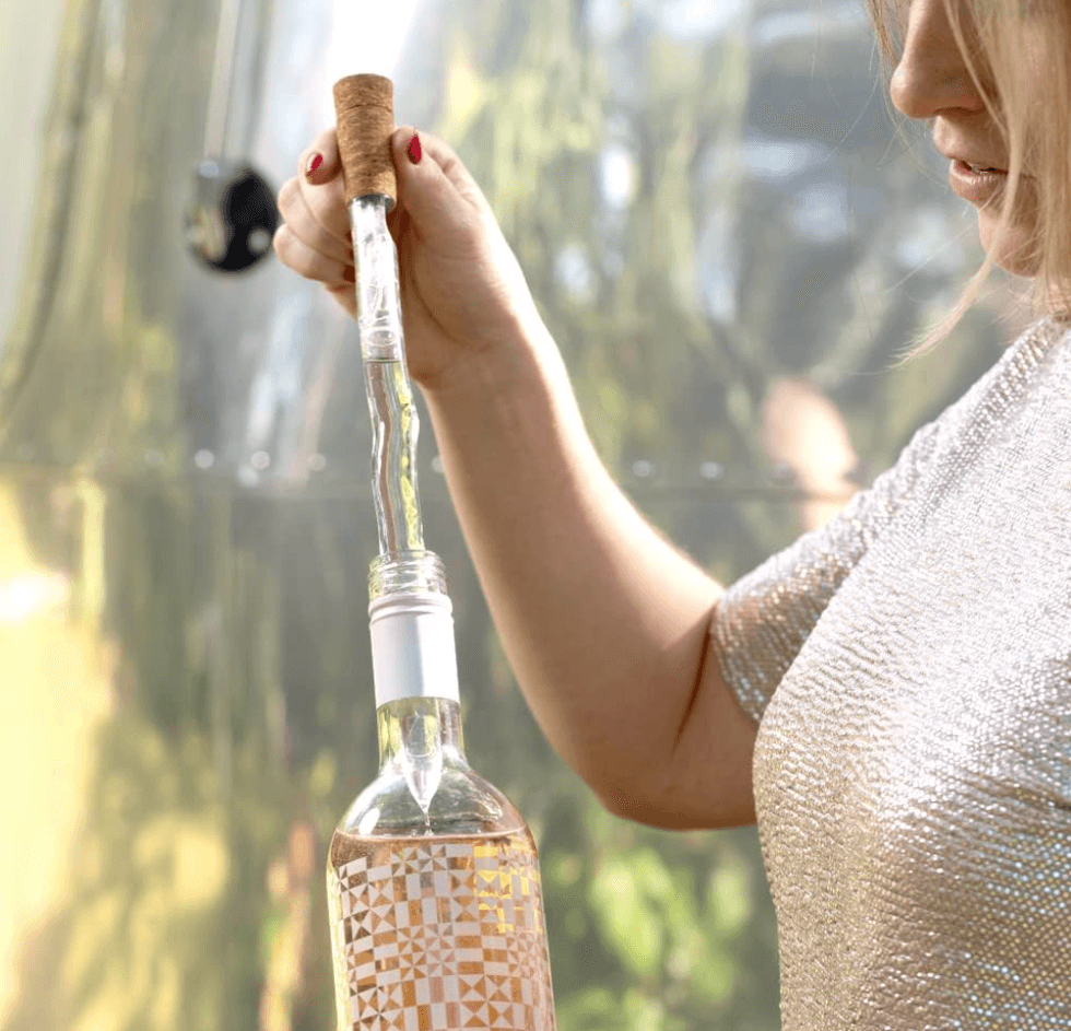 Woman holding a wine bottle with a corkscrew inserted outdoors.