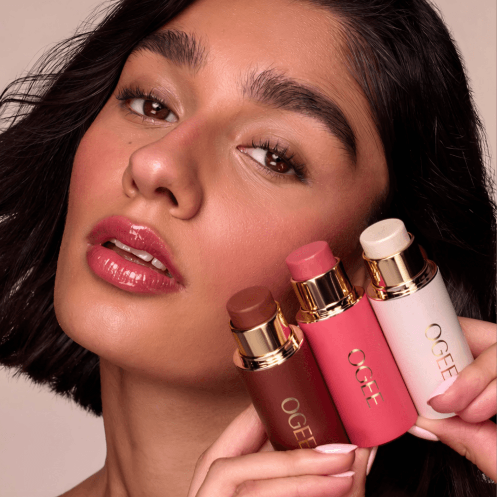 Woman holding three Ogee beauty sticks in brown, pink, and white.