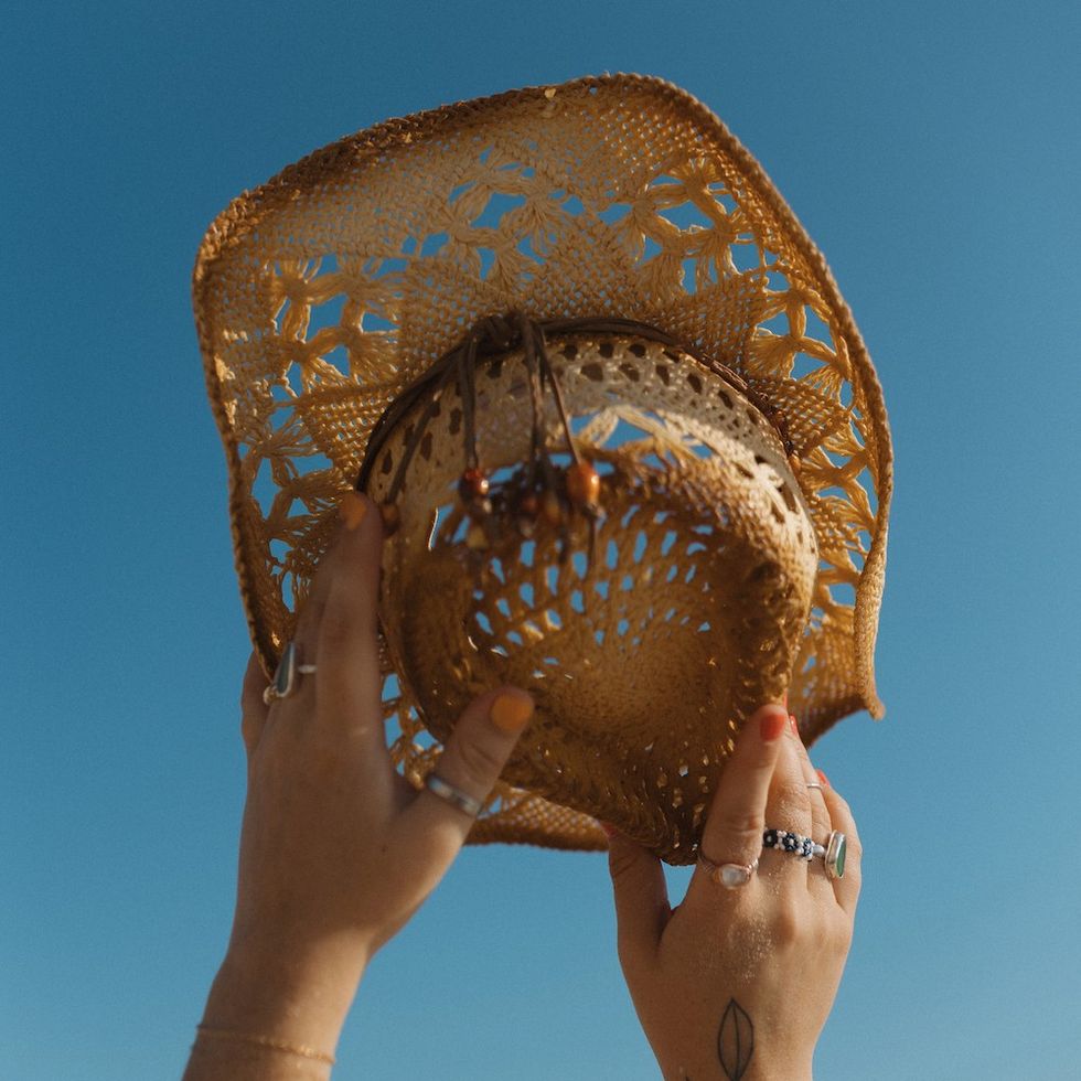 woman holding up a beachy cowgirl hat to the sky