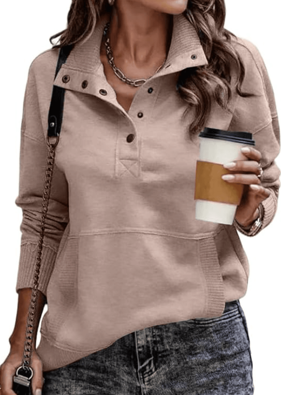 Woman in a beige pullover holding a coffee cup, wearing a chain shoulder bag.