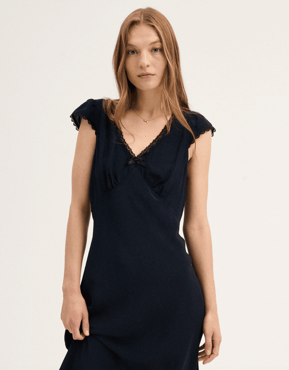 Woman in a black dress with lace trim, standing against a neutral background.