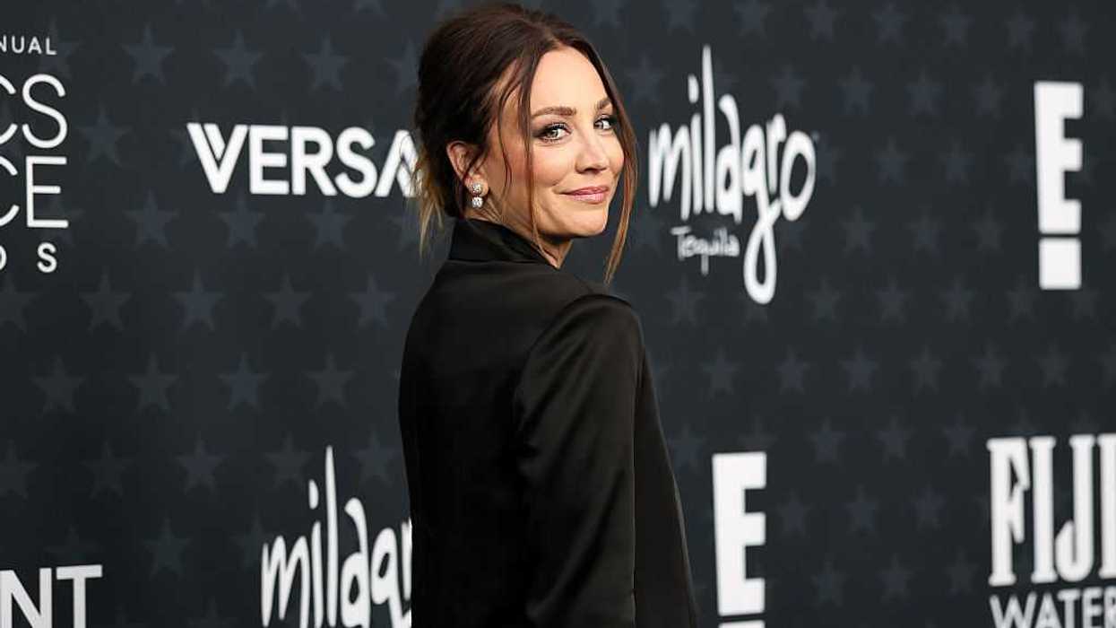 Woman in a black outfit poses at an event with sponsor logos on a dark background.