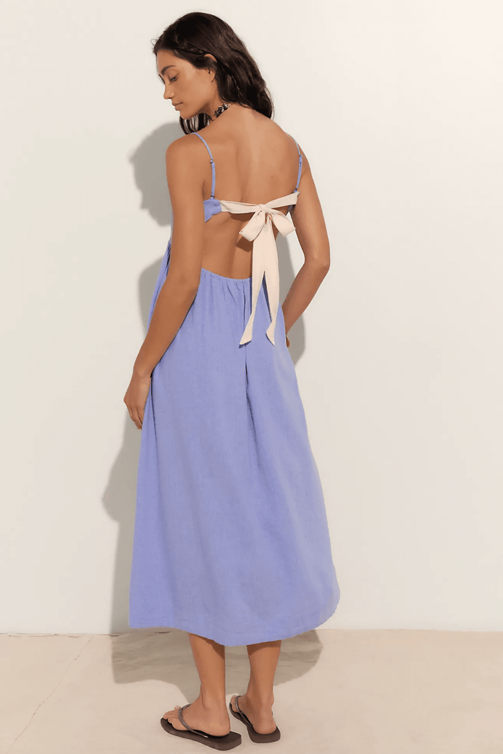 Woman in a blue dress with a back ribbon tie, standing sideways.