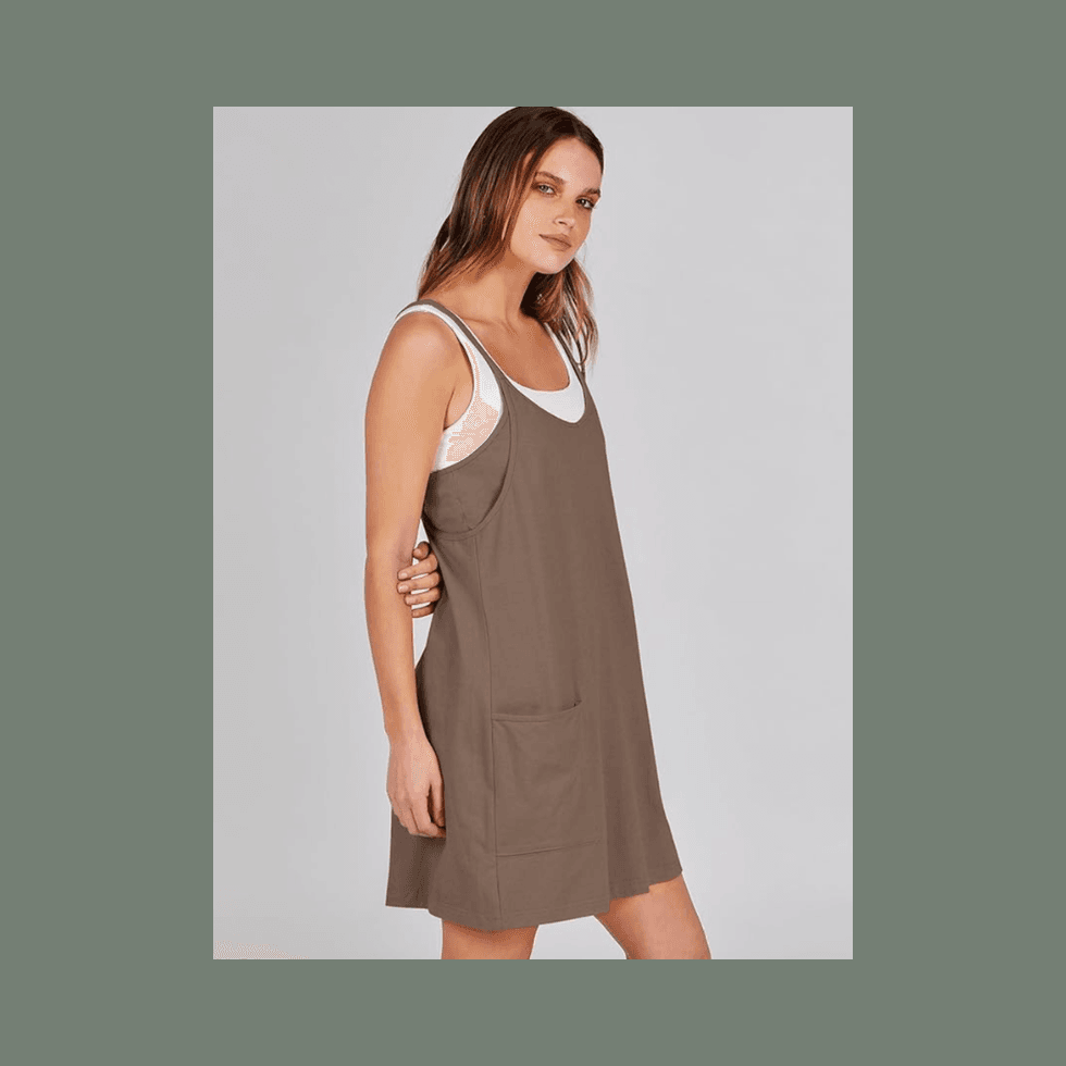 Woman in a brown sleeveless dress with a white top underneath, posing sideways.