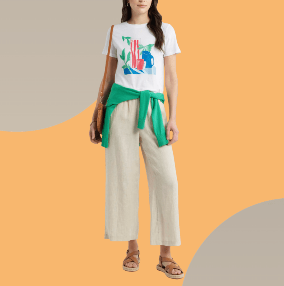 Woman in a colorful t-shirt with linen pants on an orange background.