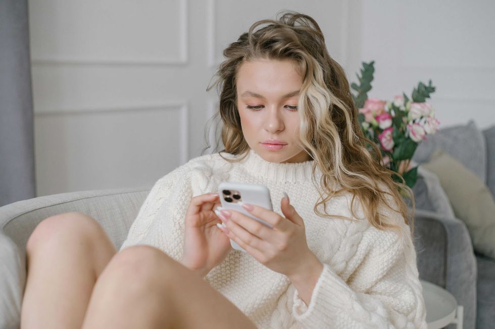 Woman in a cozy sweater using a smartphone on a couch.