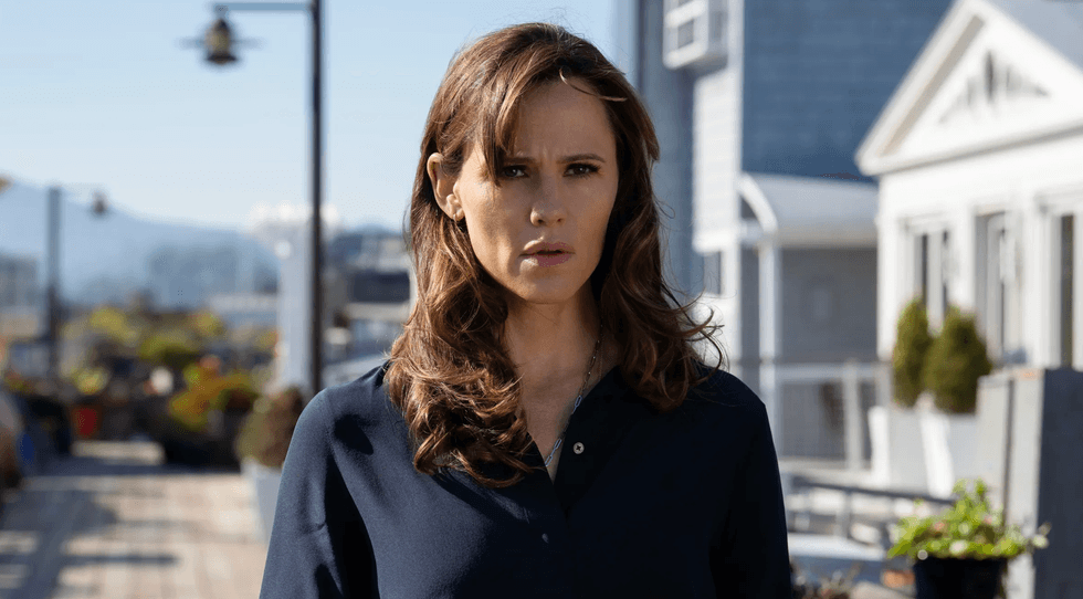 Woman in a dark shirt standing outdoors, looking serious with blurred background.