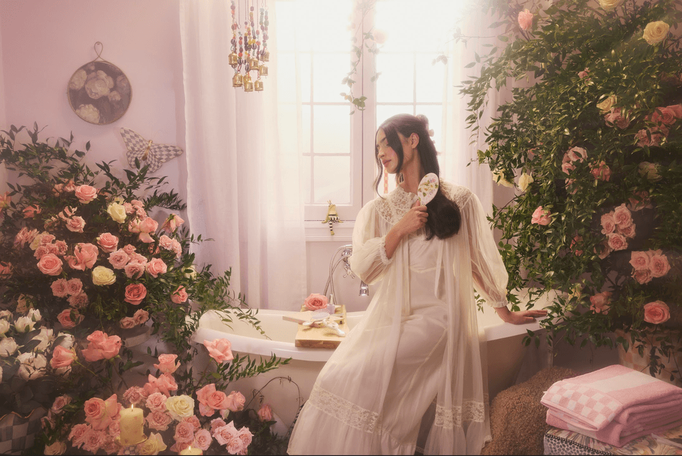 Woman in a floral-adorned bathroom, gently brushing hair by a sunlit window.