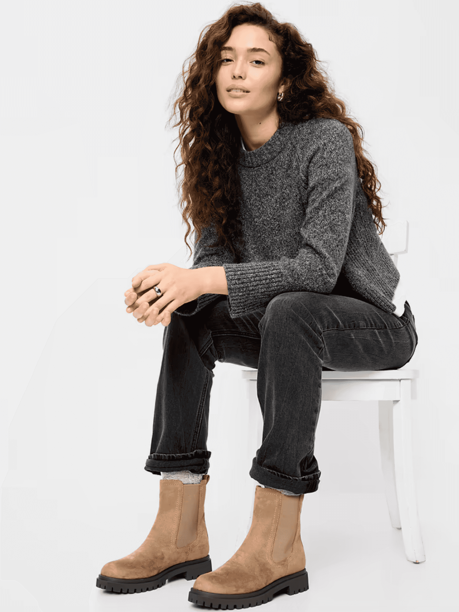 Woman in a gray sweater and jeans sits on a chair, wearing tan ankle boots.