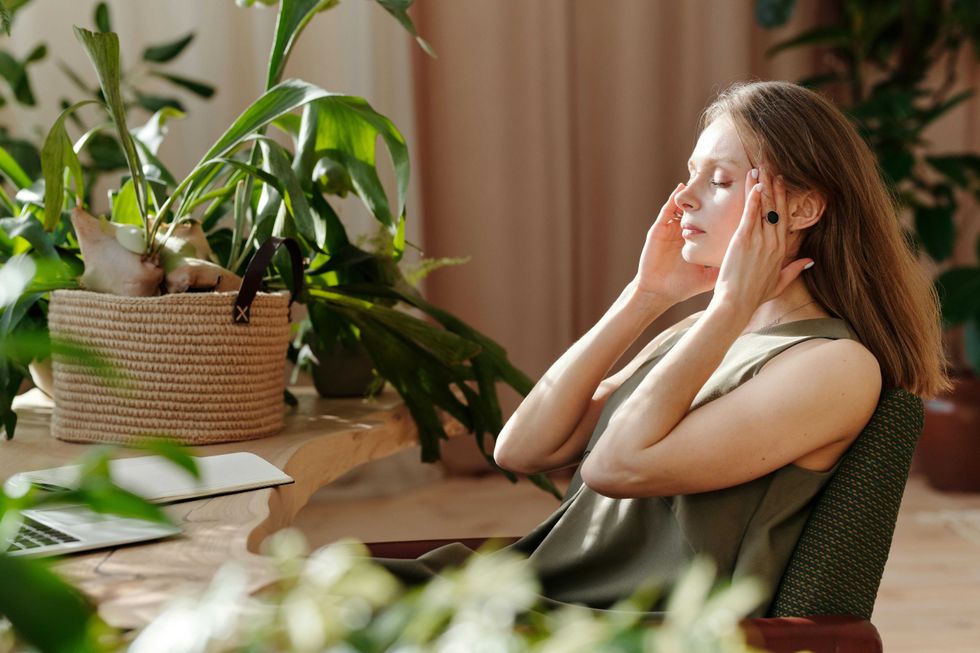 Woman in a green chair relaxing with eyes closed, surrounded by indoor plants.