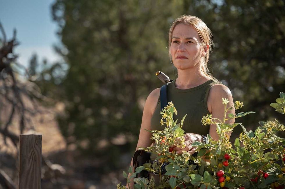 Woman in a green top stands outside near plants with a thoughtful expression.