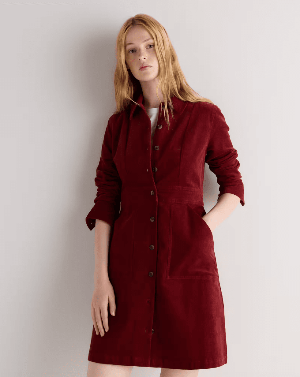 Woman in a maroon buttoned dress poses against a light background.