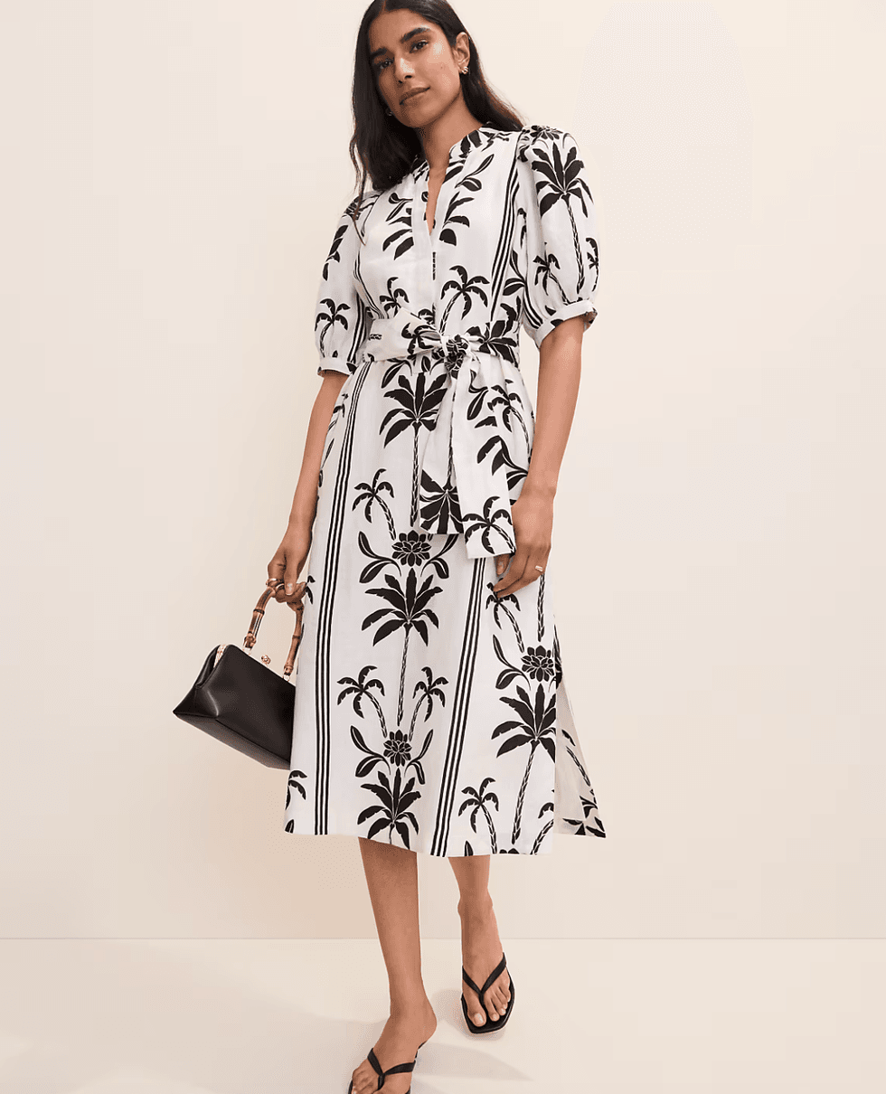 Woman in a palm print dress with puff sleeves, holding a black handbag.