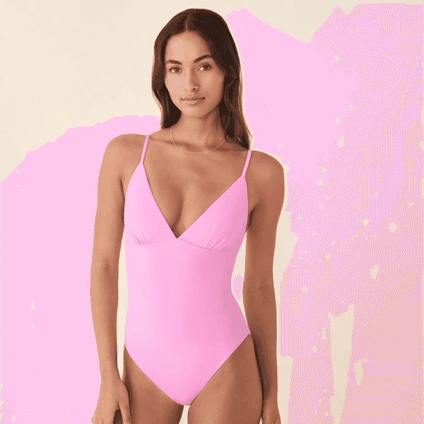 Woman in a pink one-piece swimsuit with thin straps against a neutral background.