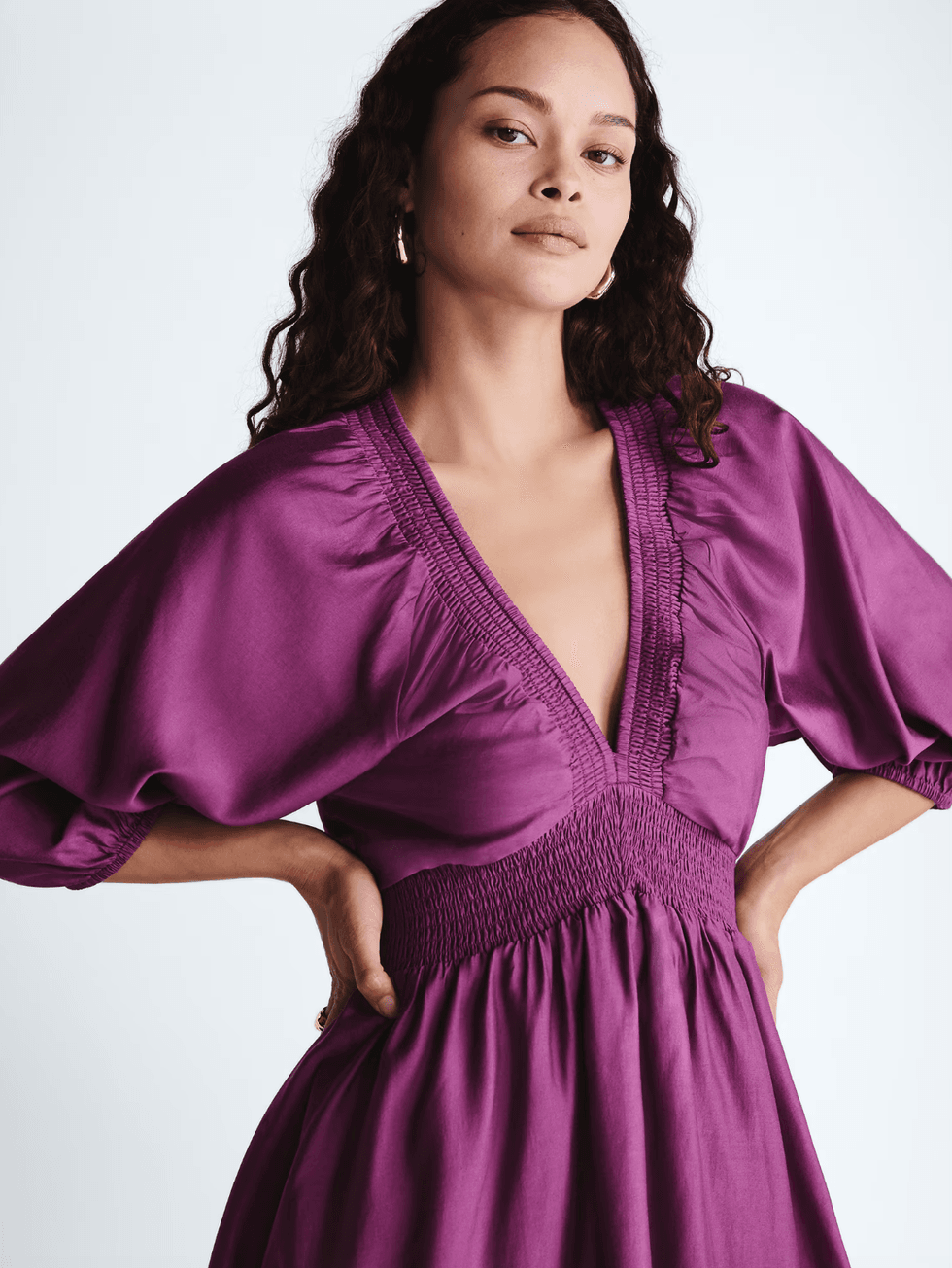 Woman in a purple V-neck dress with smocked details and puffed sleeves.