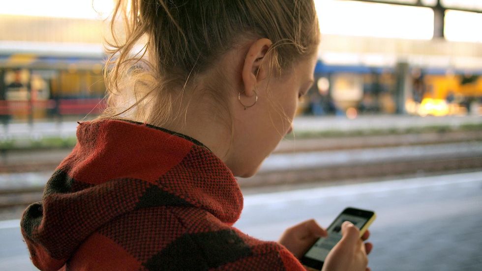 woman in a red and black hoodie checking her phone in a train station traveling alone