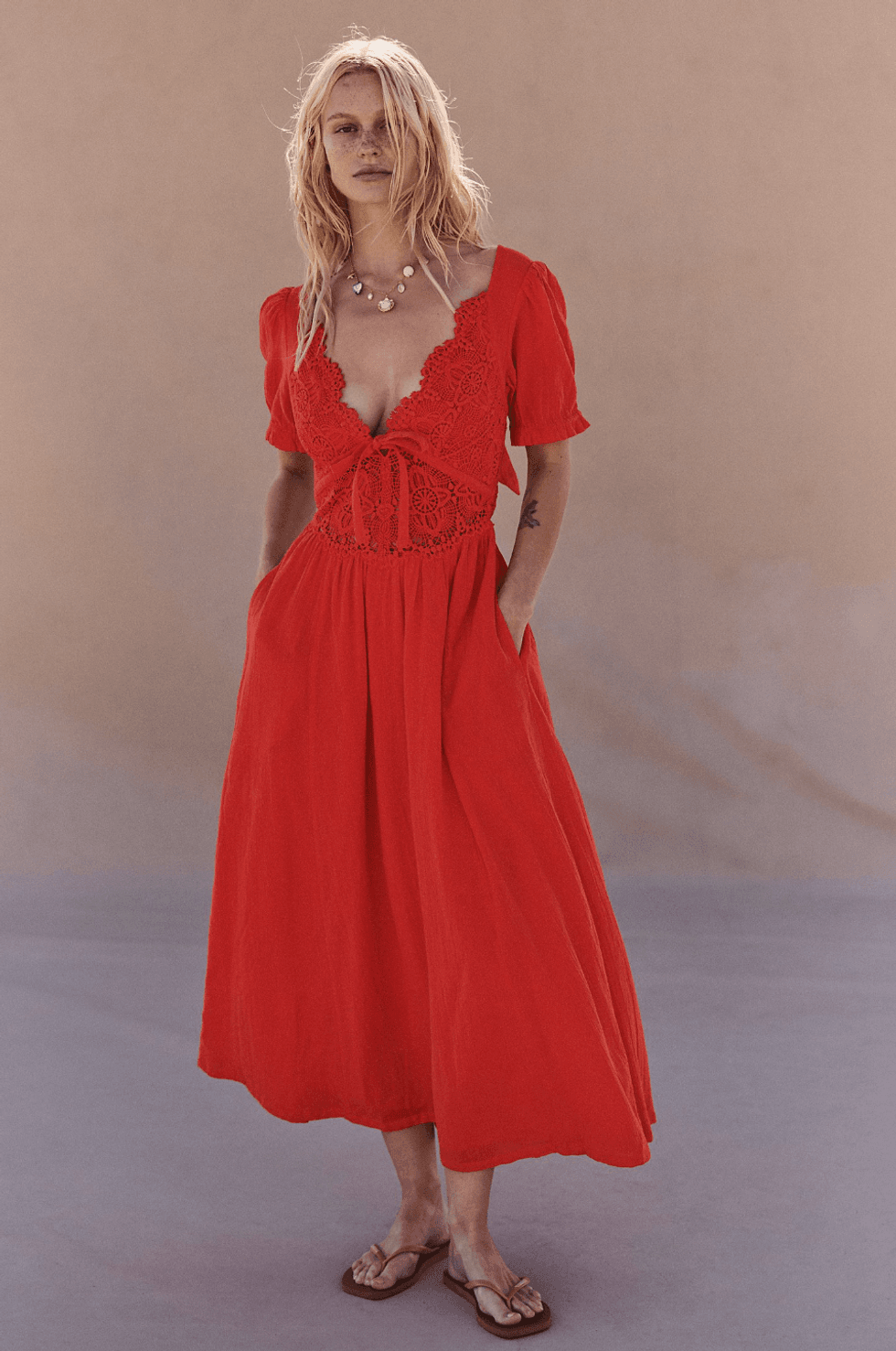 Woman in a red lace dress with flip-flops, standing against a neutral background.