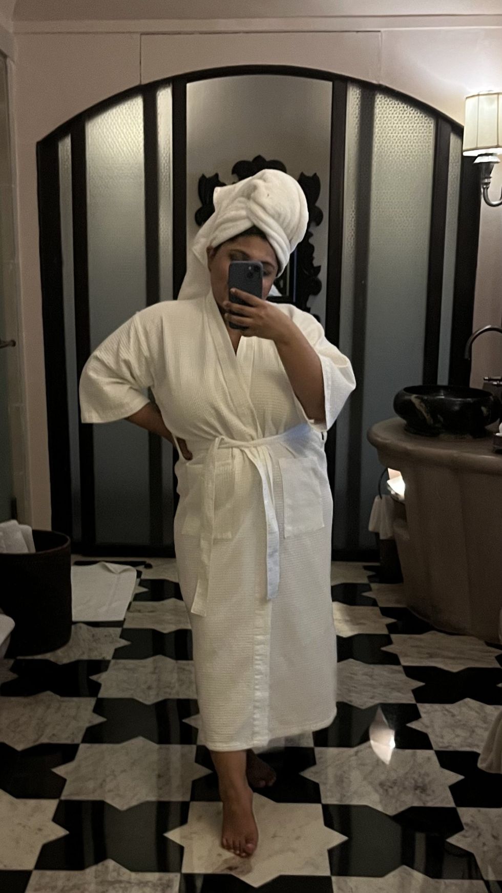 woman in a robe with her hair in a towel taking a mirror selfie