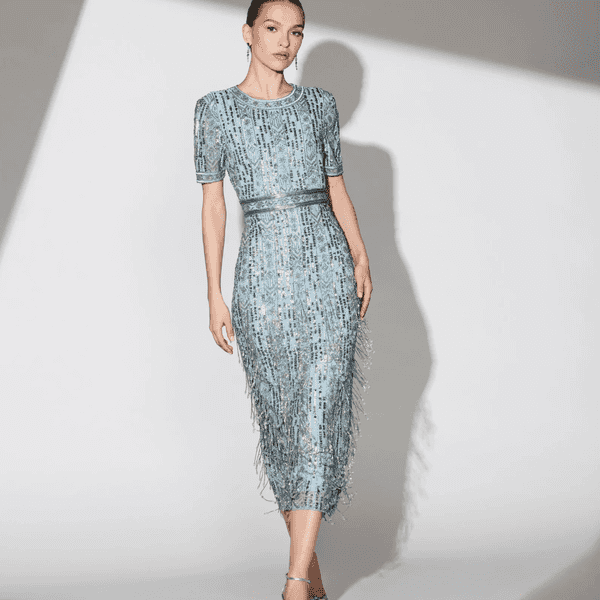 Woman in a shimmering blue dress with fringe details, posing on a lit set.