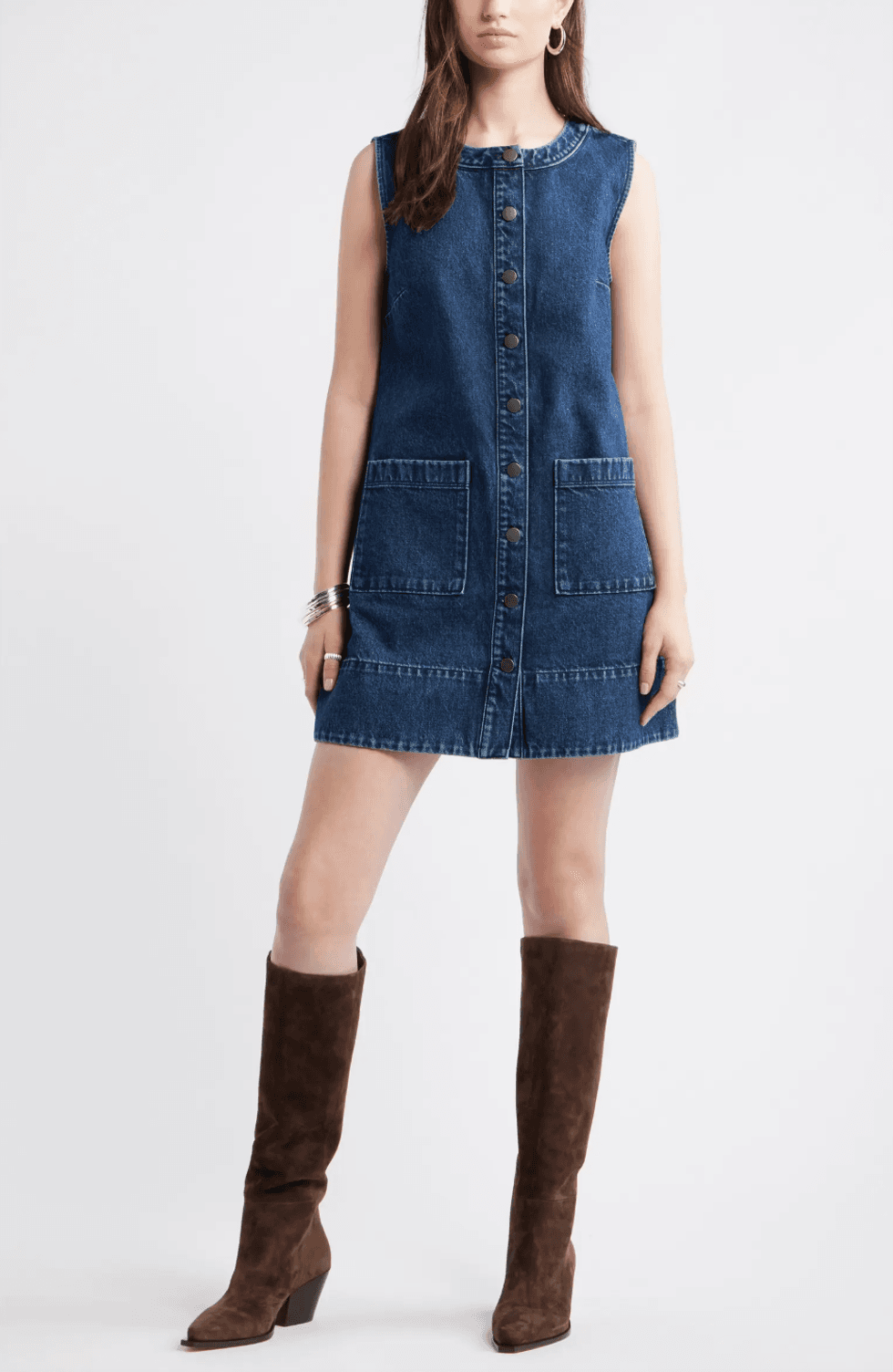 Woman in a sleeveless denim dress with knee-high brown boots.