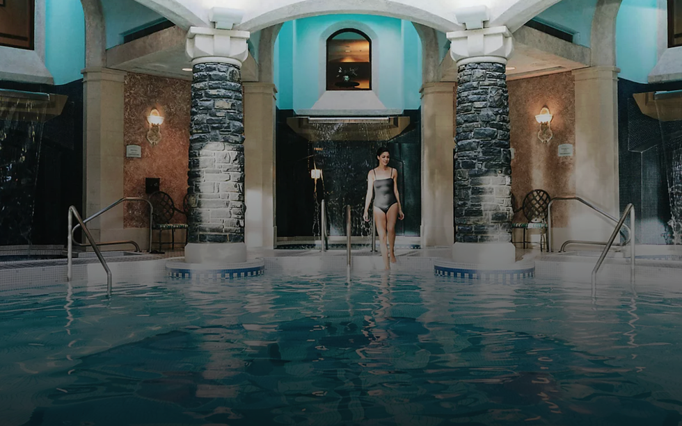 Woman in a swimsuit at a luxurious indoor pool with stone pillars and arched decor.
