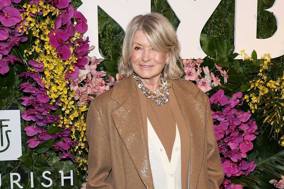 Woman in a tan outfit smiling in front of a floral backdrop.