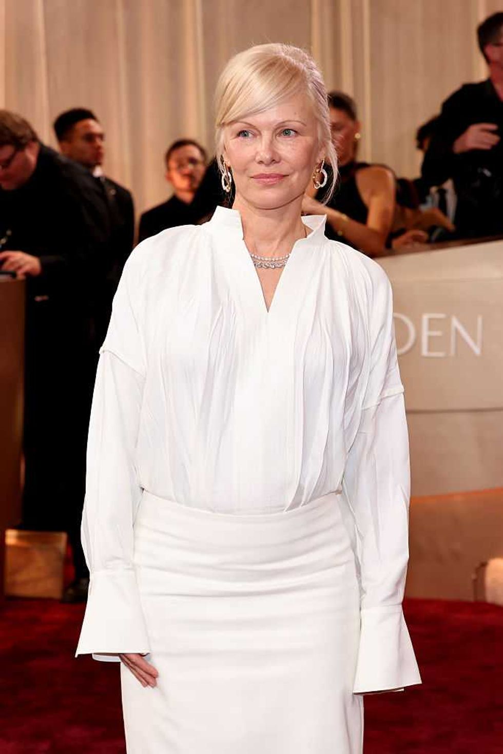 Woman in a white dress poses on a red carpet at an event.