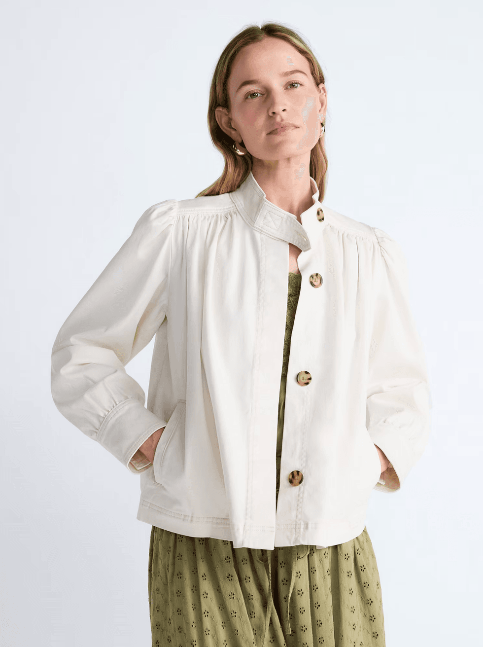 Woman in a white jacket over a green dress, hands in pockets.
