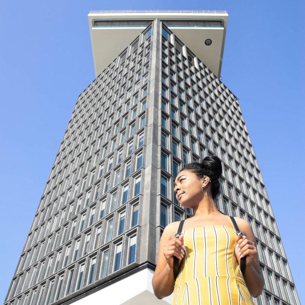 woman in a yellow striped dress stands outside a building with lots of windows traveling alone