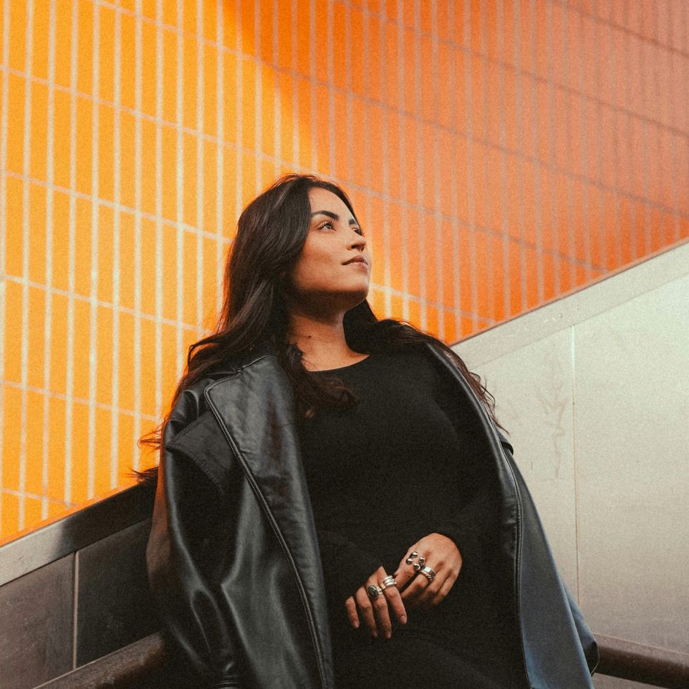 woman in an all back outfit standing in front of an orange wall