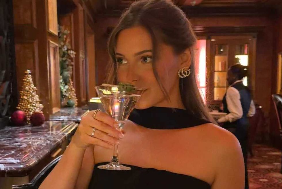 Woman in an elegant restaurant enjoying a cocktail, festive decor in background.