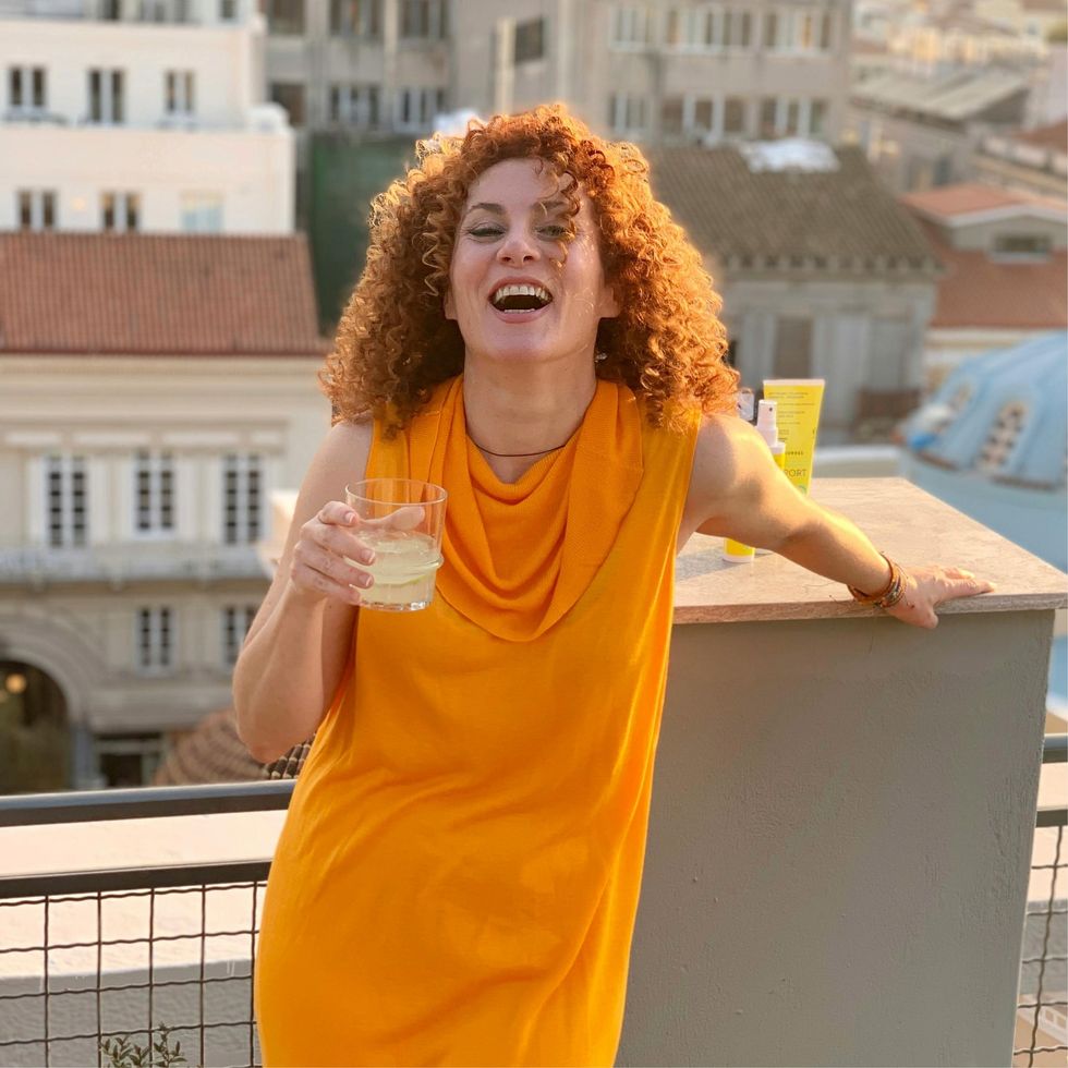 woman in an orange dress, laughing and holding a cocktail