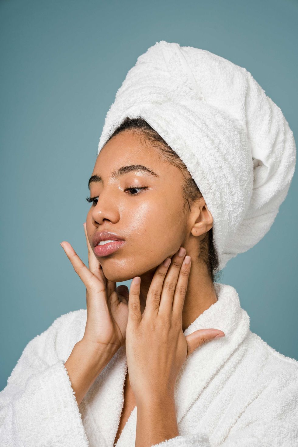 Woman in bathrobe and towel touches her face against a blue background.