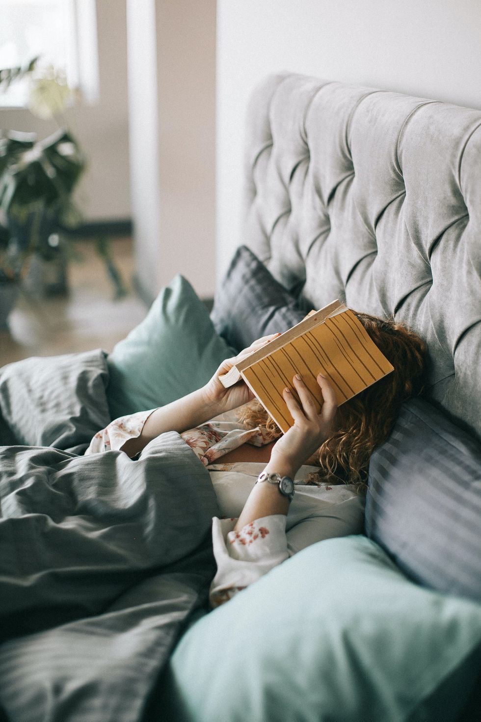 woman in bed with a book over her face