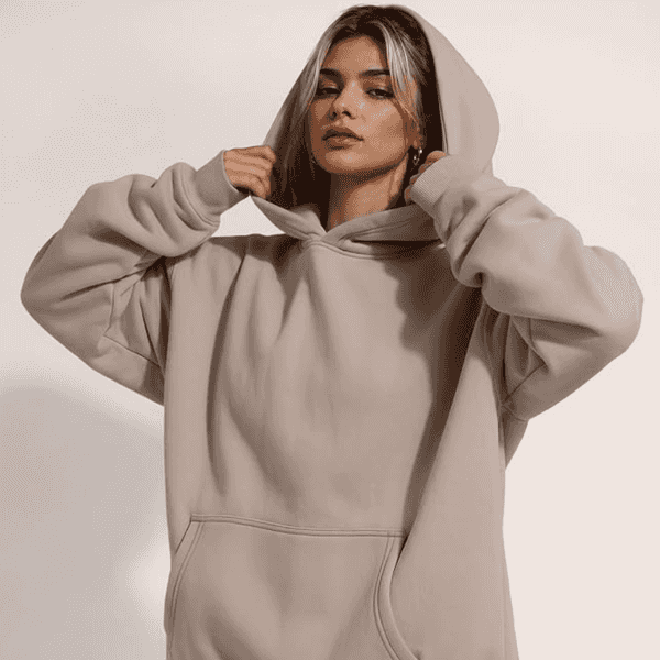 Woman in beige hoodie adjusting the hood, posing confidently.