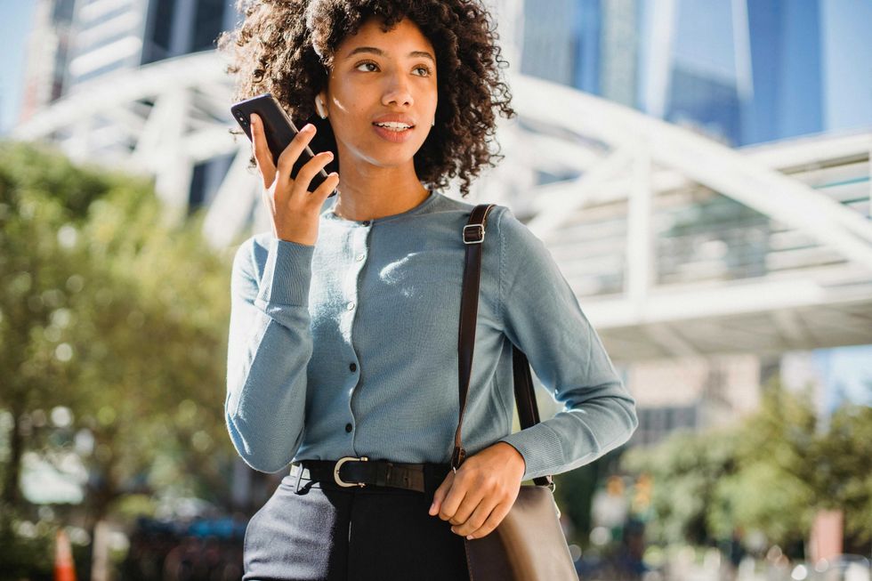 Woman in blue cardigan holding smartphone, walking in urban setting.