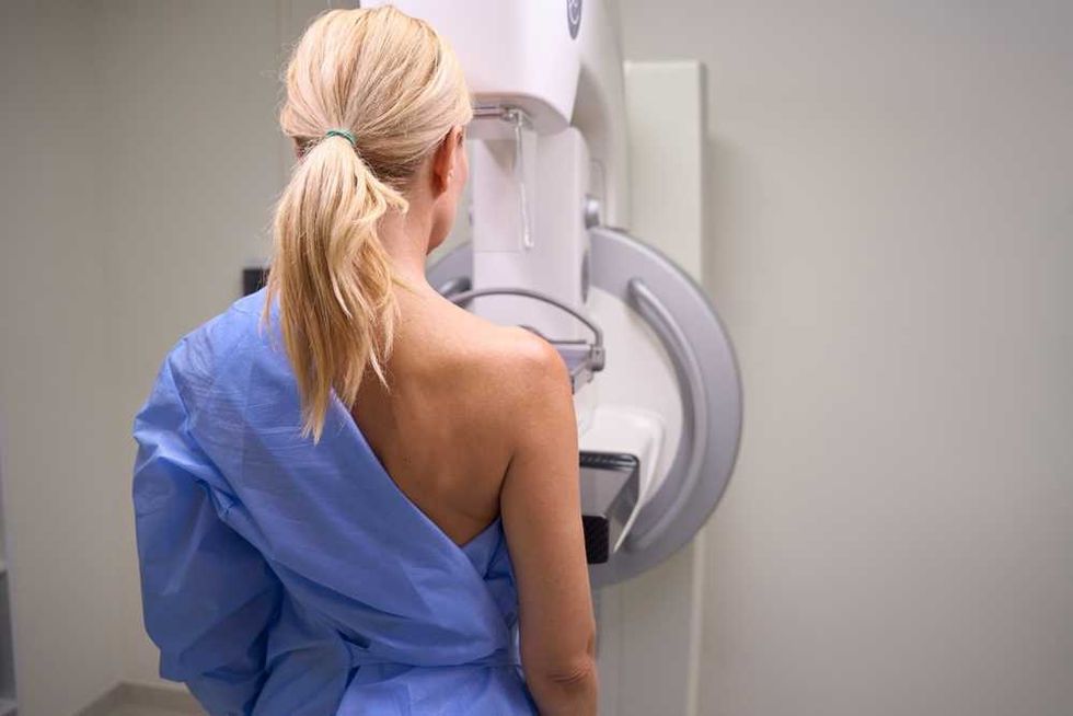 Woman in blue gown undergoing a mammogram in a medical setting.