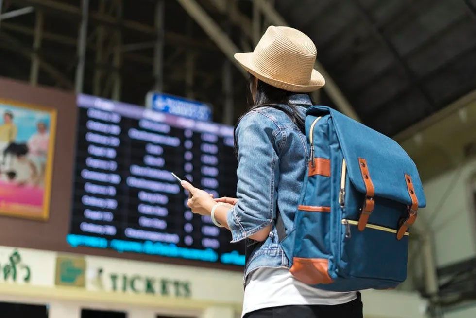 woman in blue jean jacket and straw hat traveling with blue backpack at train station or airport