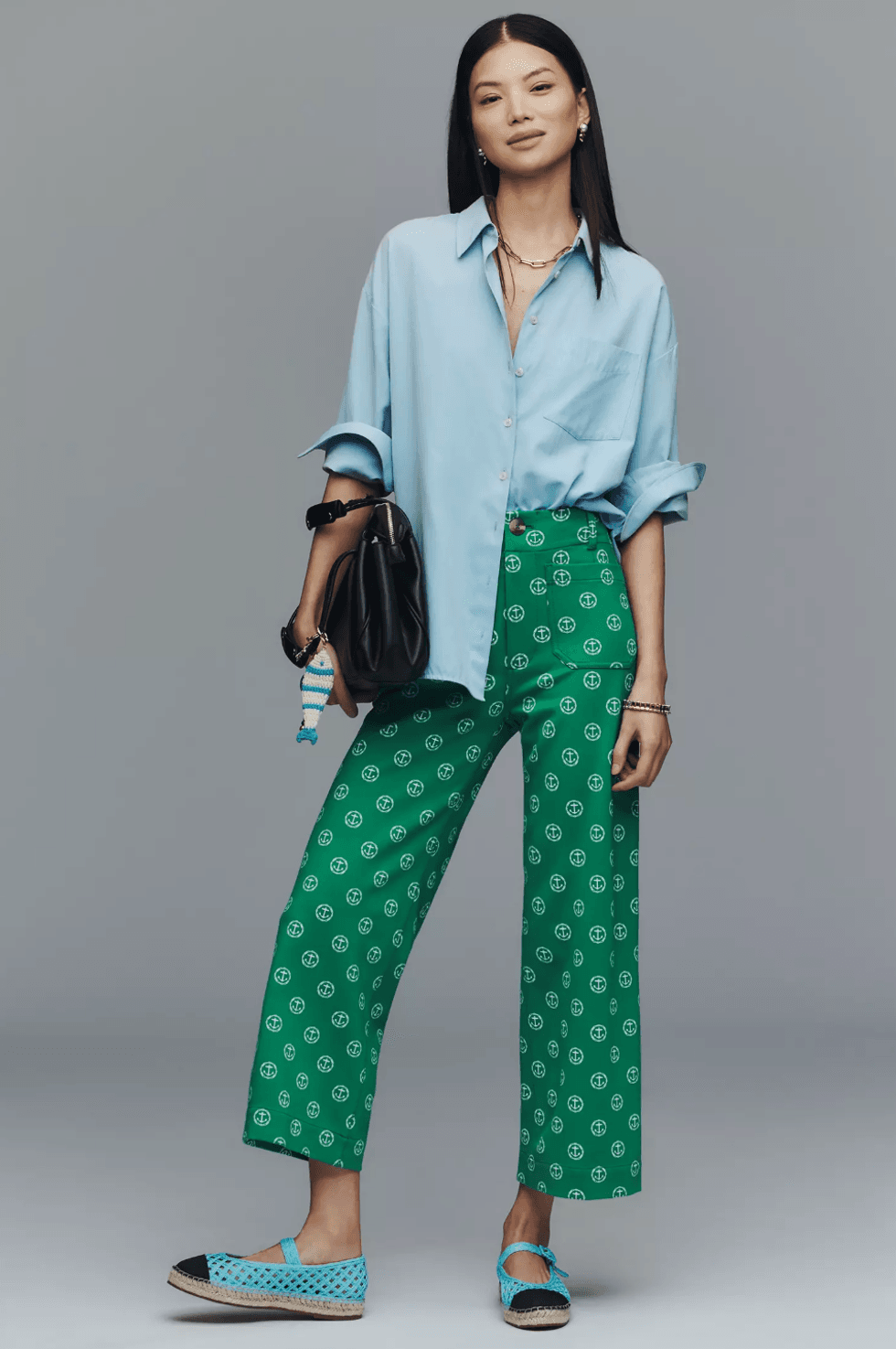 Woman in blue shirt, green patterned pants, and blue shoes holding a black bag.