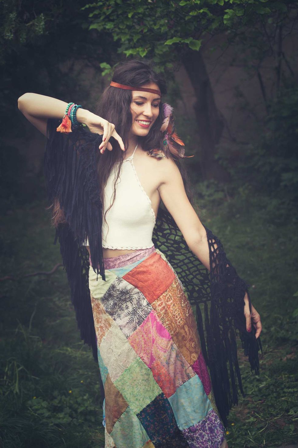 Woman in boho attire with patchwork skirt, dancing outdoors.