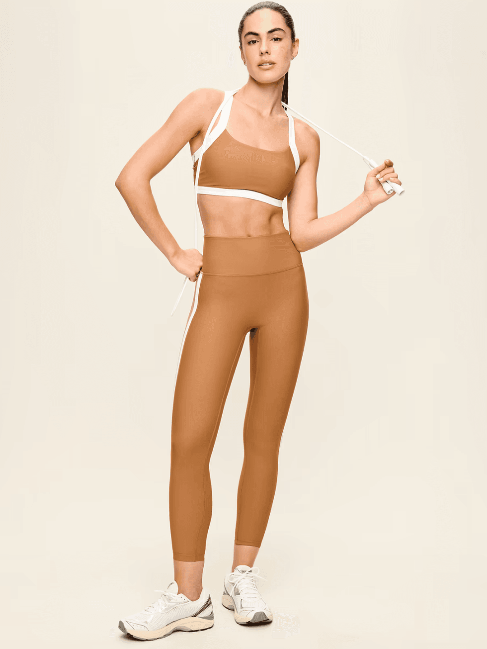 Woman in brown activewear holding a jump rope, standing against a plain background.