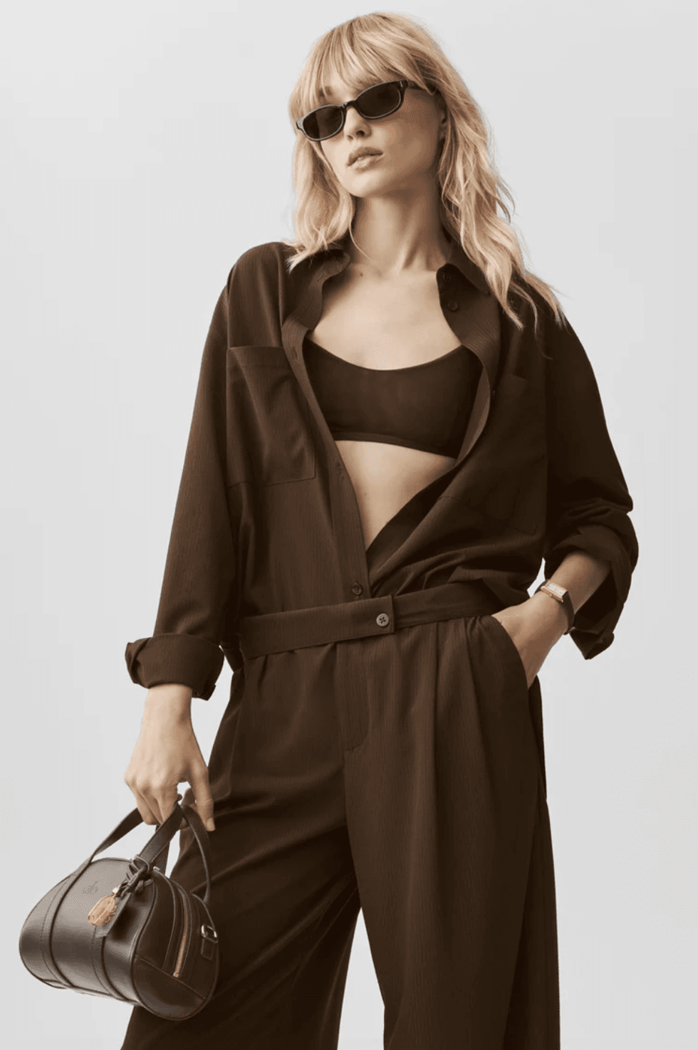 Woman in dark oversized outfit holding a handbag, wearing sunglasses.