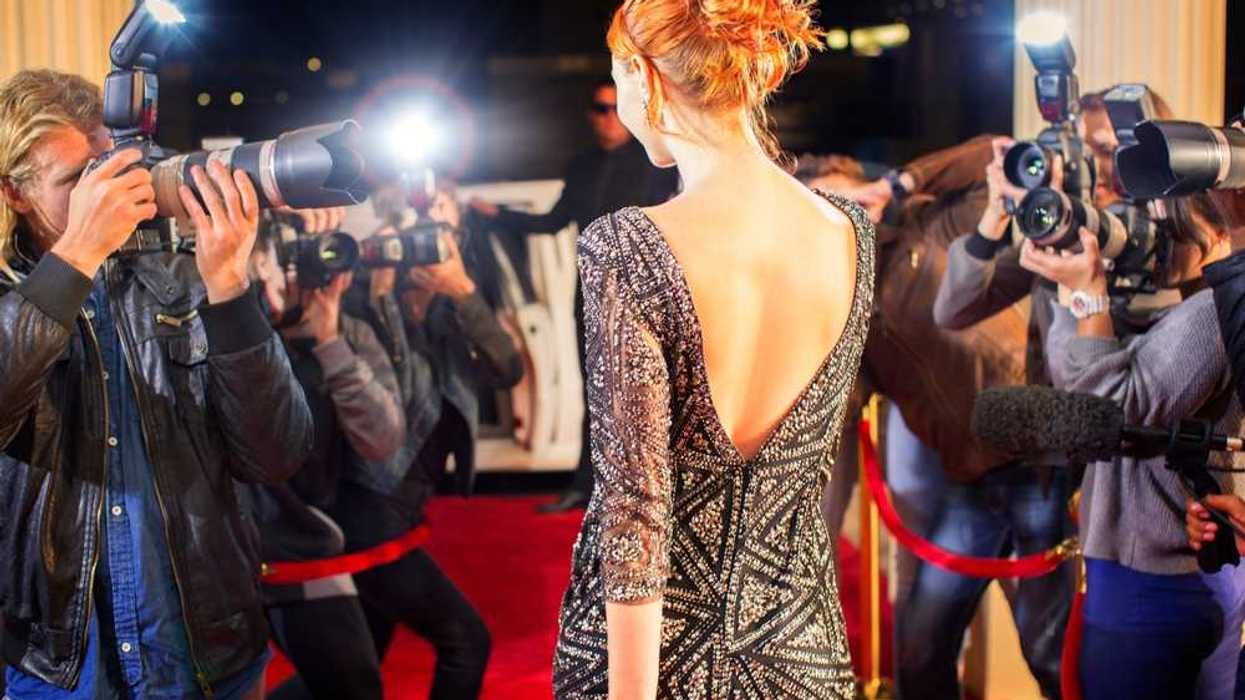 Woman in elegant dress on red carpet facing paparazzi flashbulbs.