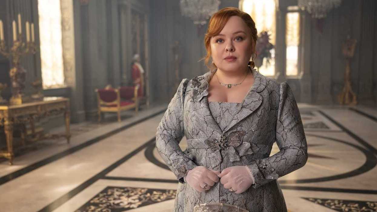 Woman in formal attire stands in an ornate room with chandeliers and candelabras.