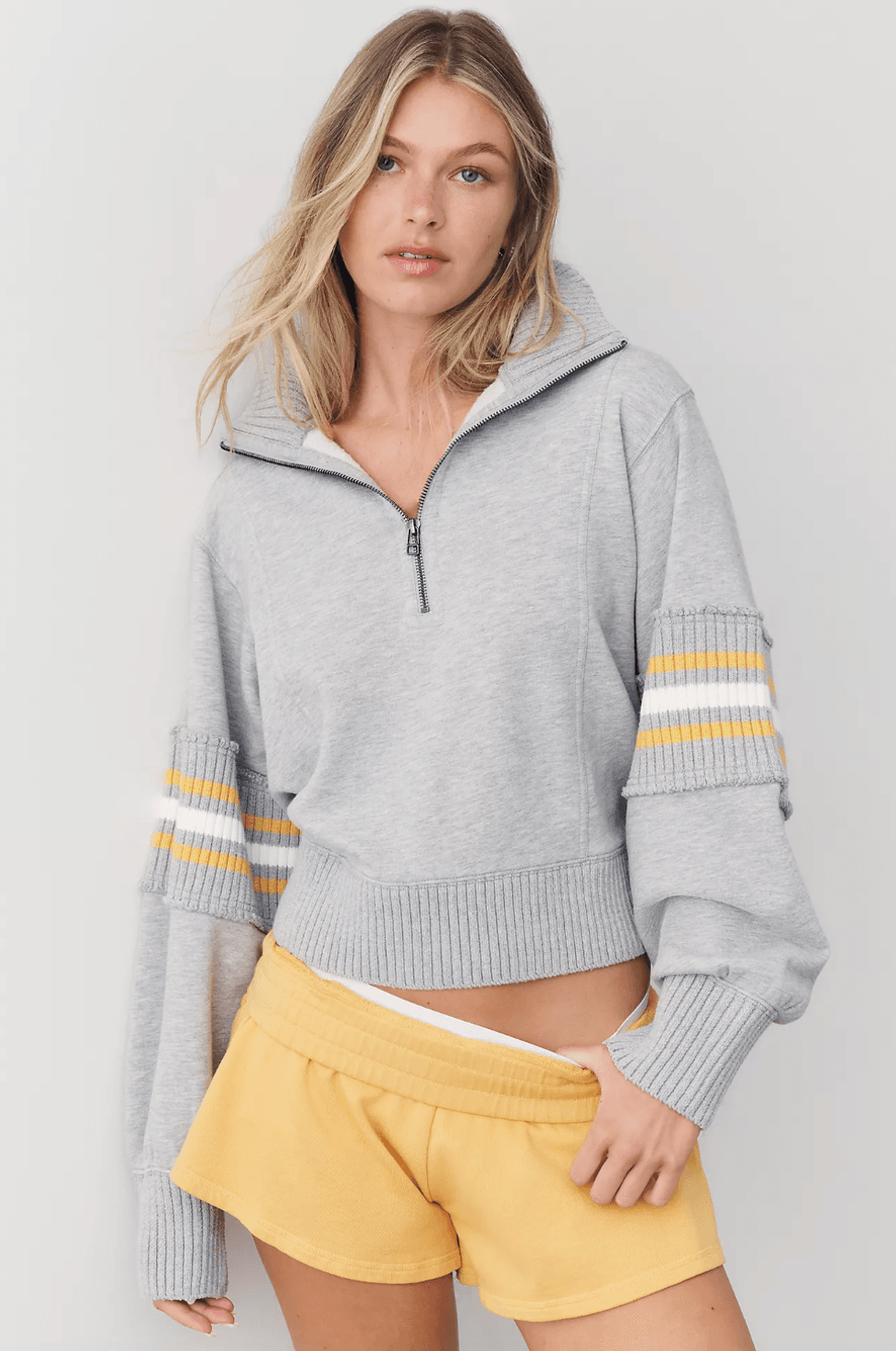 Woman in gray hoodie and yellow shorts with hand in pocket.